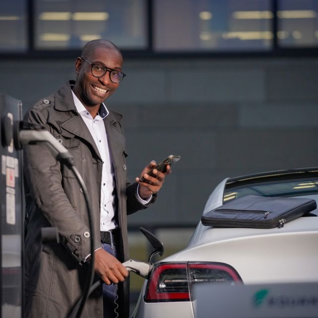 oplossingen-e-mobility-man-met-telefoon-en-laadkabel-bij-auto-lachend-1280x890.jpg